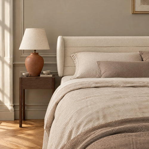 Tête de lit à oreilles en tissu Bagatelle écru dans une chambre, avec table de chevet et lampe