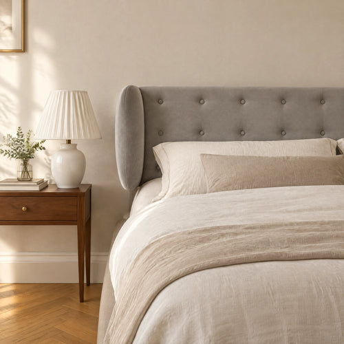 Tête de lit boutonnée à oreilles en velours Auteuil gris clair dans une chambre, avec table de chevet et lampe
