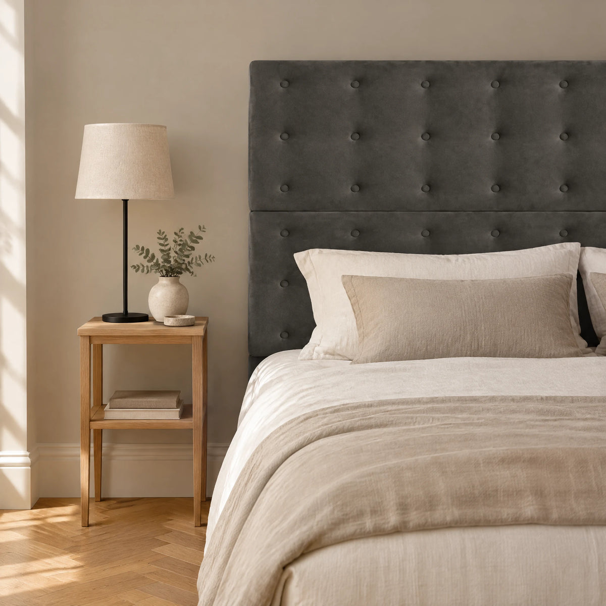 Tête de lit haute boutonnée en velours Invalides gris anthracite dans une chambre, avec table de chevet et lampe