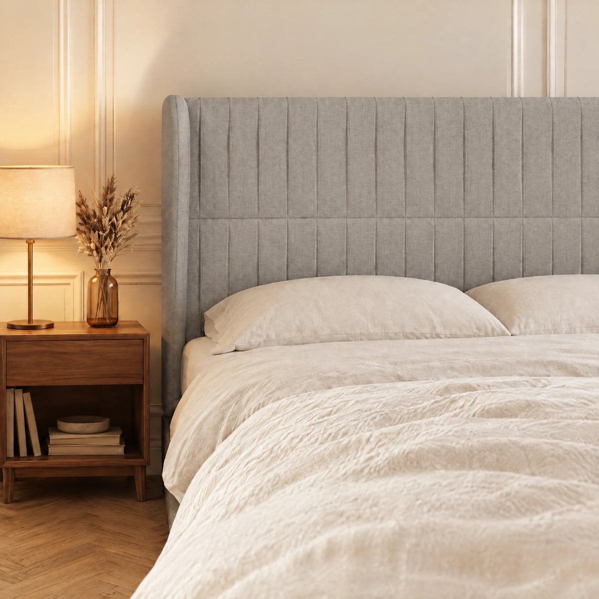 Tête de lit haute cannelée à oreilles en tissu Friedland gris clair dans une chambre, avec table de chevet et lampe