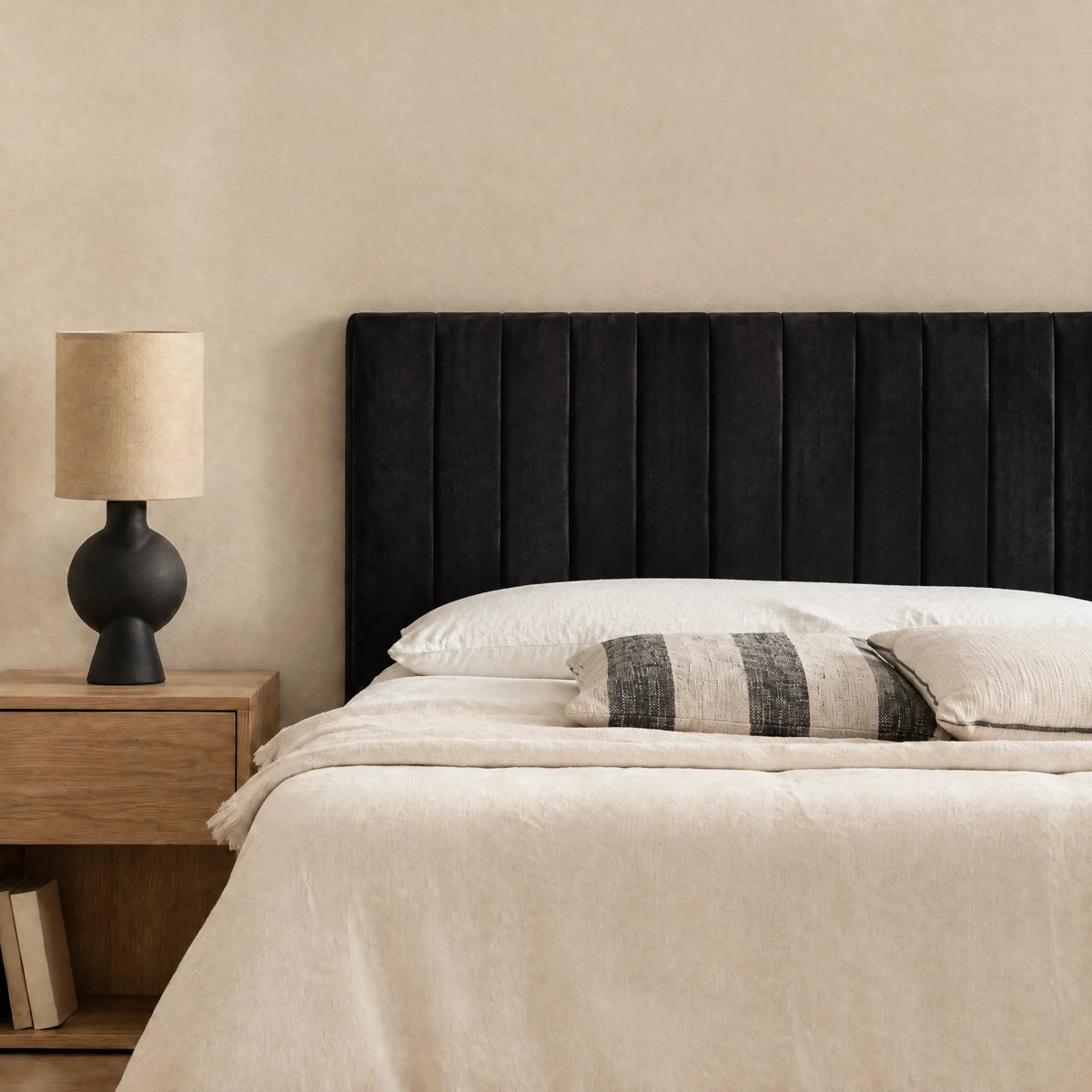 Tête de lit en velours Madeleine noir dans une chambre, avec table de chevet et lampe
