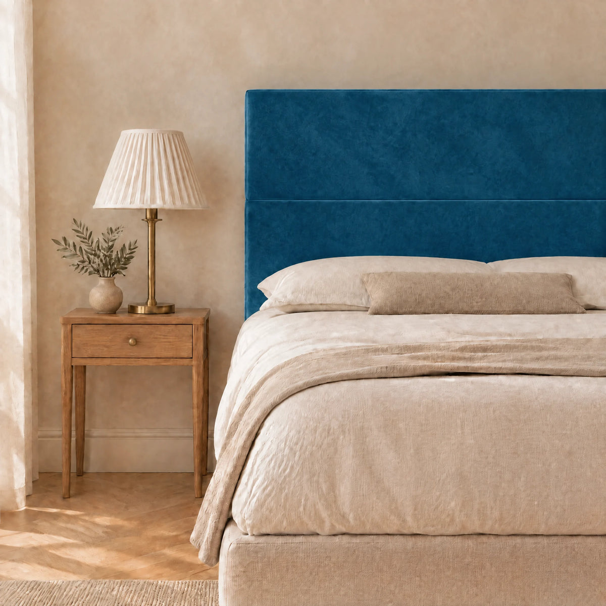 Tête de lit haute en velours lisse Châtelet bleu canard dans une chambre, avec table de chevet et lampe
