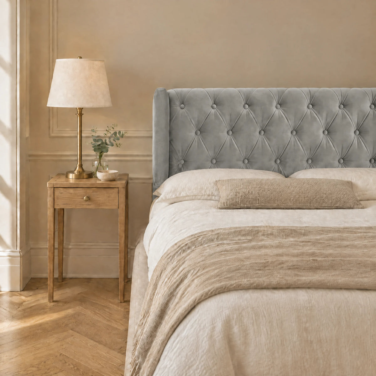 Tête de lit capitonnée à oreilles en velours Montaigne gris clair dans une chambre, avec table de chevet et lampe