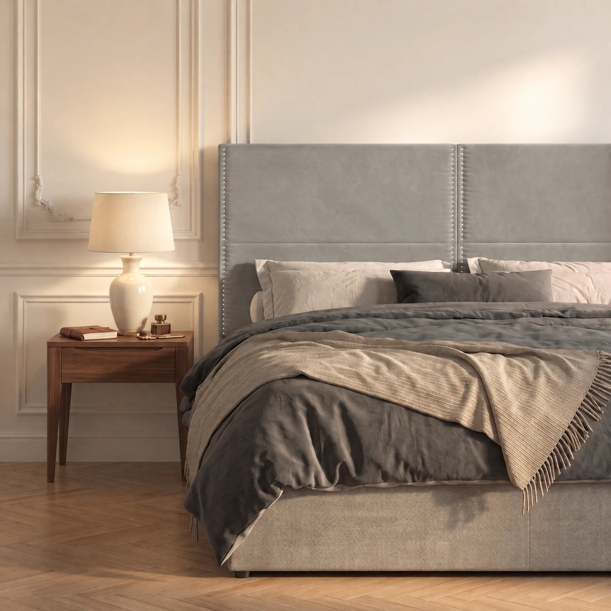 Tête de lit haute cloutée en velours Matignon gris clair dans une chambre, avec table de chevet et lampe