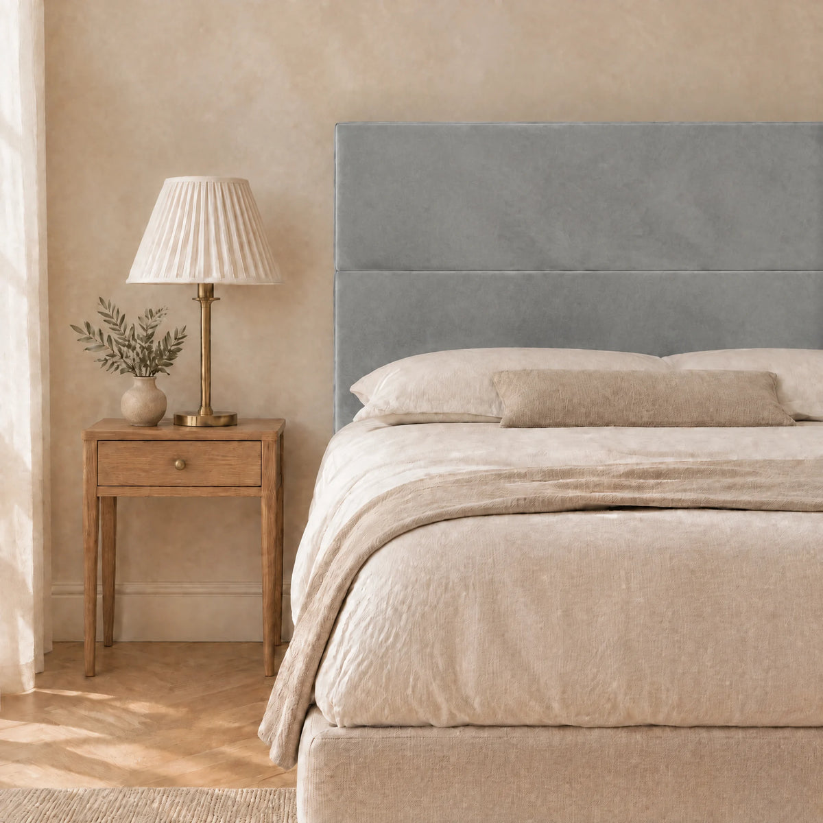 Tête de lit haute en velours lisse Châtelet gris clair dans une chambre, avec table de chevet et lampe