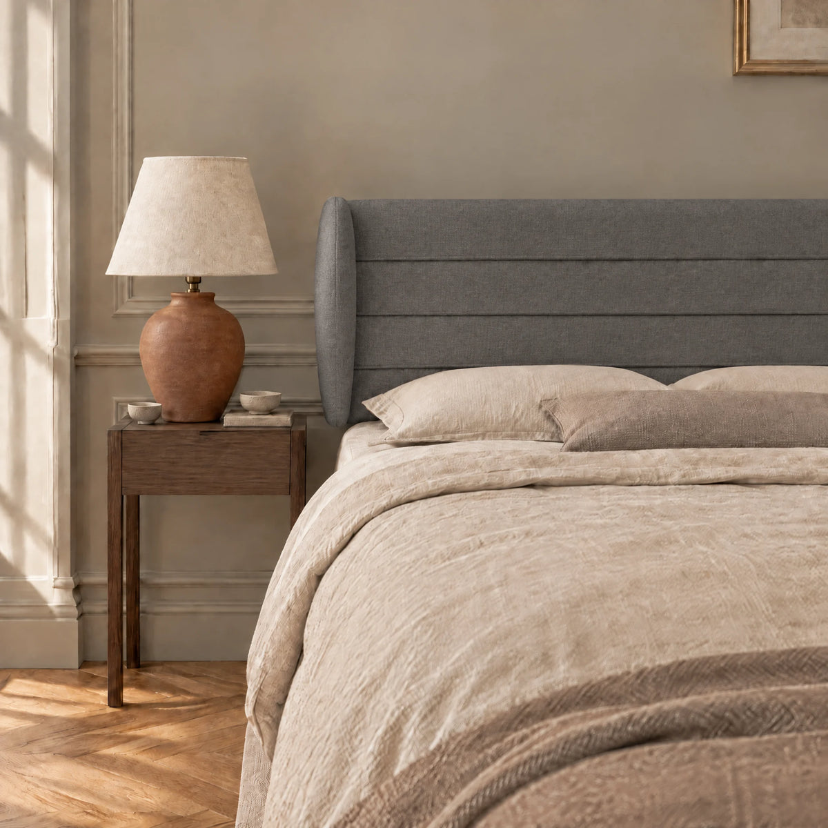 Tête de lit à oreilles en tissu Bagatelle gris anthracite dans une chambre, avec table de chevet et lampe