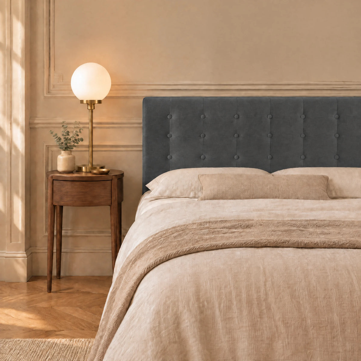 Tête de lit boutonnée en velours Dauphine gris anthracite dans une chambre, avec table de chevet et lampe