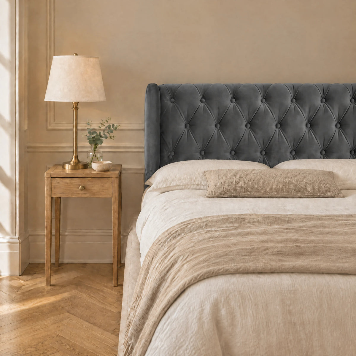 Tête de lit capitonnée à oreilles en velours Montaigne gris anthracite dans une chambre, avec table de chevet et lampe