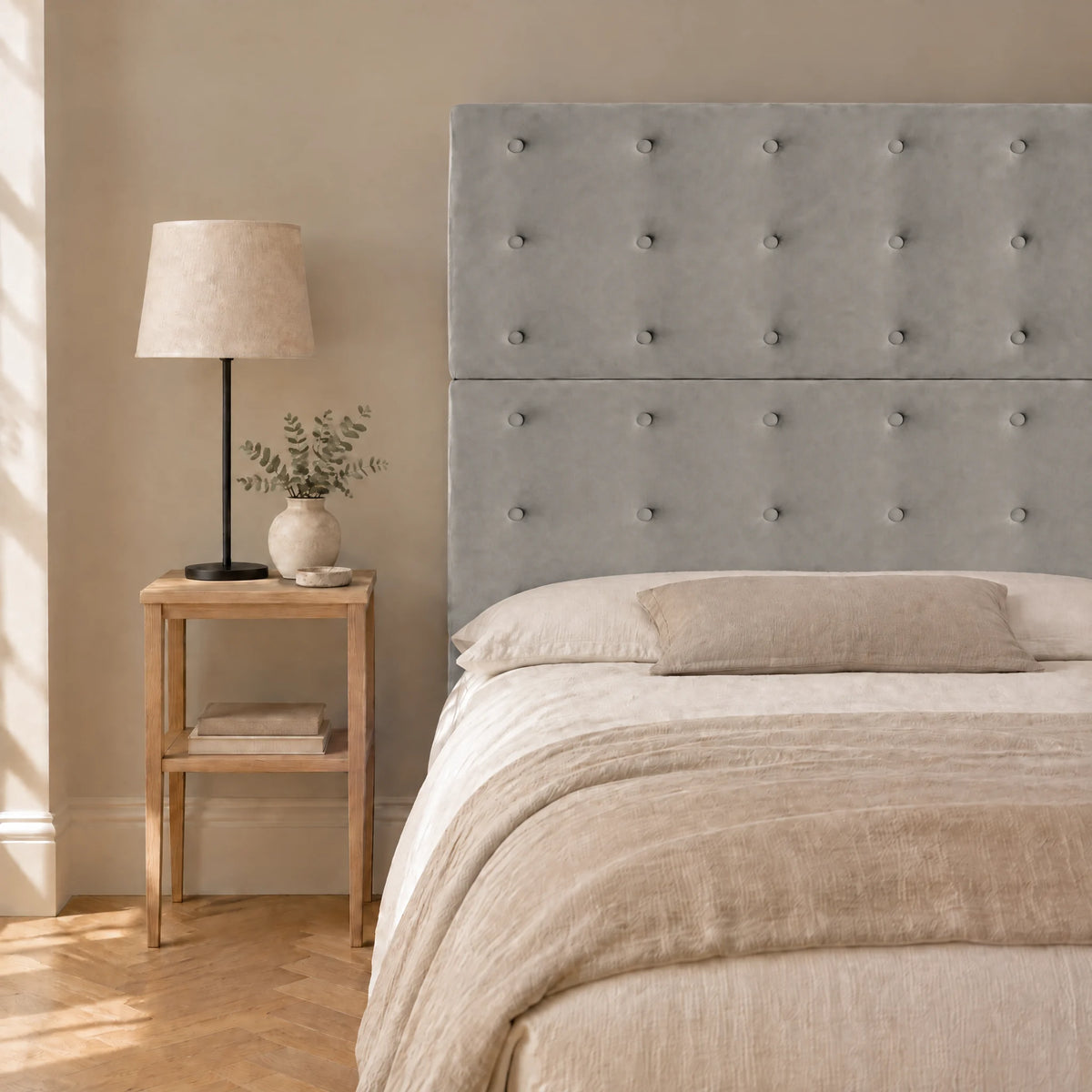 Tête de lit haute boutonnée en velours Invalides gris clair dans une chambre, avec table de chevet et lampe