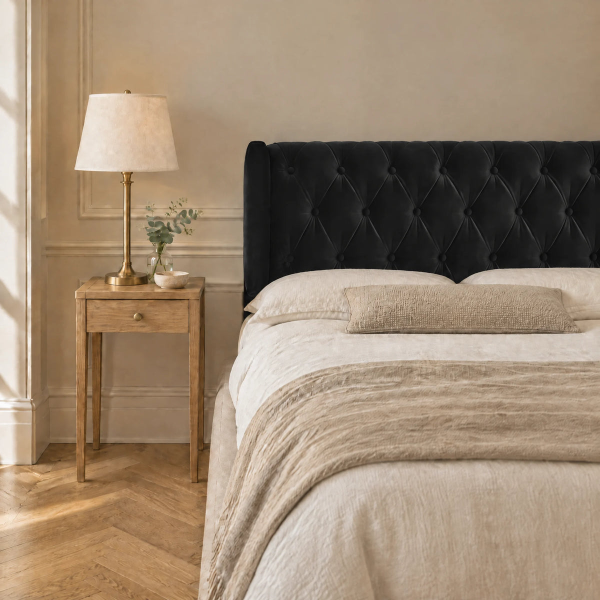 Tête de lit capitonnée à oreilles en velours Montaigne noir dans une chambre, avec table de chevet et lampe