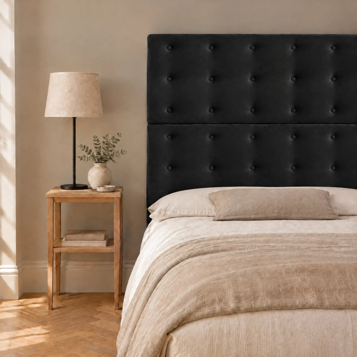 Tête de lit haute boutonnée en velours Invalides noir dans une chambre, avec table de chevet et lampe