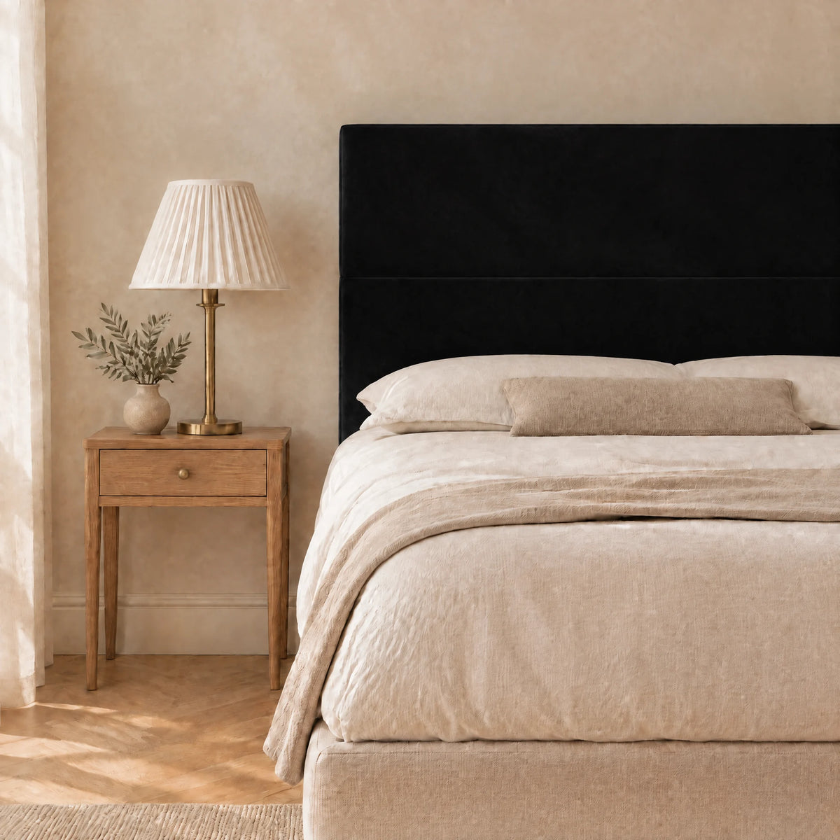 Tête de lit haute en velours lisse Châtelet noir dans une chambre, avec table de chevet et lampe
